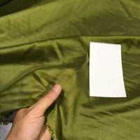 A hand displays the Solid Color Ramie Fabric By The Yard from Longan Craft—a super lightweight, breathable lyocell ramie material in green—next to a rectangular white card for texture and color comparison, ideal for blouses.
