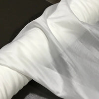 A close-up of Solid Color Ramie Fabric by the yard from Longan Craft, showcasing its super lightweight and breathable Lyocell ramie material draped over a soft, rounded surface. The smooth white fabric forms gentle folds and shadows against a dark background, highlighting its elegant texture—ideal for making airy blouses.