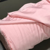 A close-up of a roll of Longan Craft’s Solid Color Ramie Fabric By The Yard in light pink, featuring rough, unfinished edges and partially unrolled on a dark surface. This super lightweight lyocell ramie material is breathable and showcases both texture and softness—ideal for blouses.