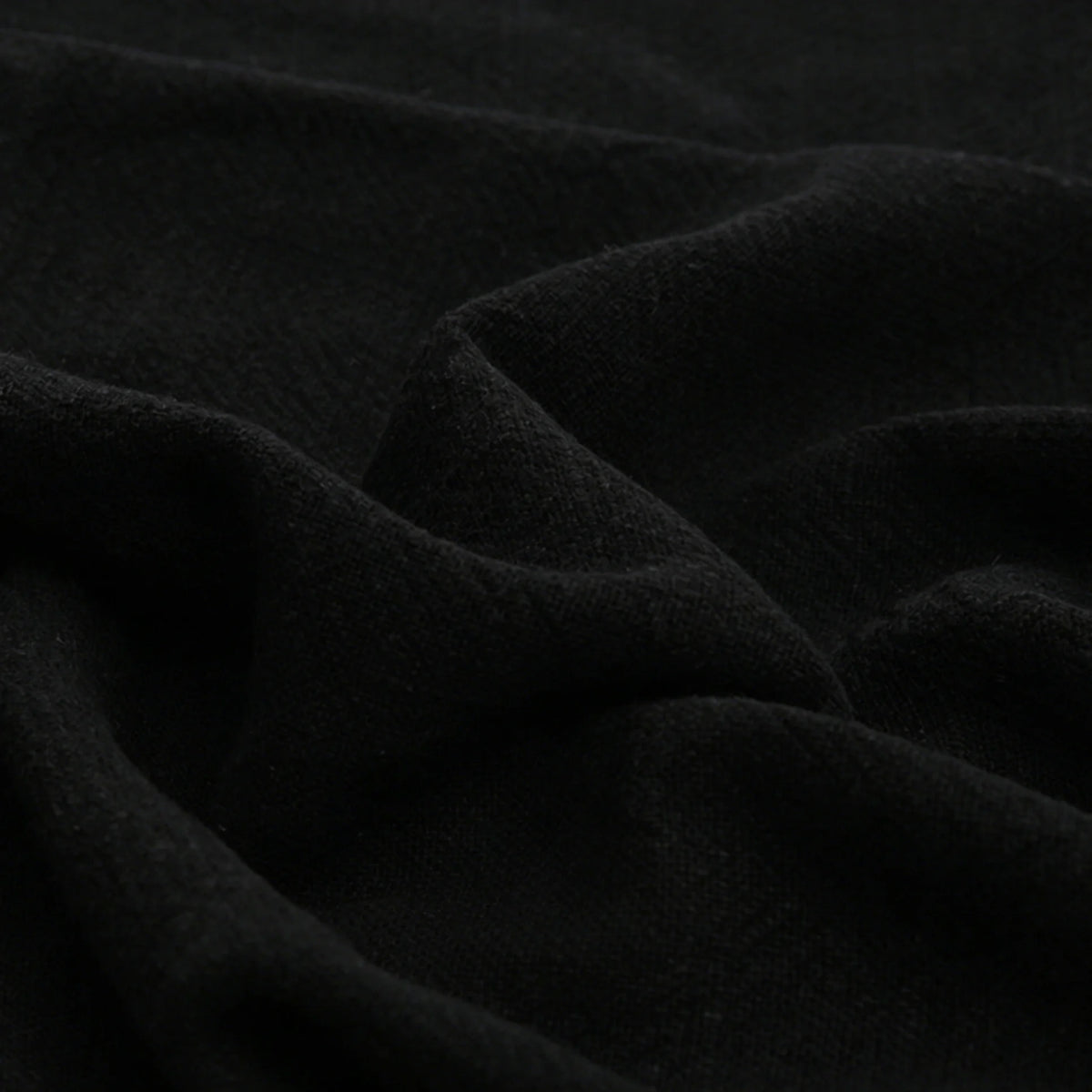 Close-up of Longan Craft’s Solid Color Rayon Linen Fabric By The Yard—thick, washed slub viscose with a soft, textured surface in solid black, ideal for dresses and clothing. Subtle folds create gentle shadows and highlights.