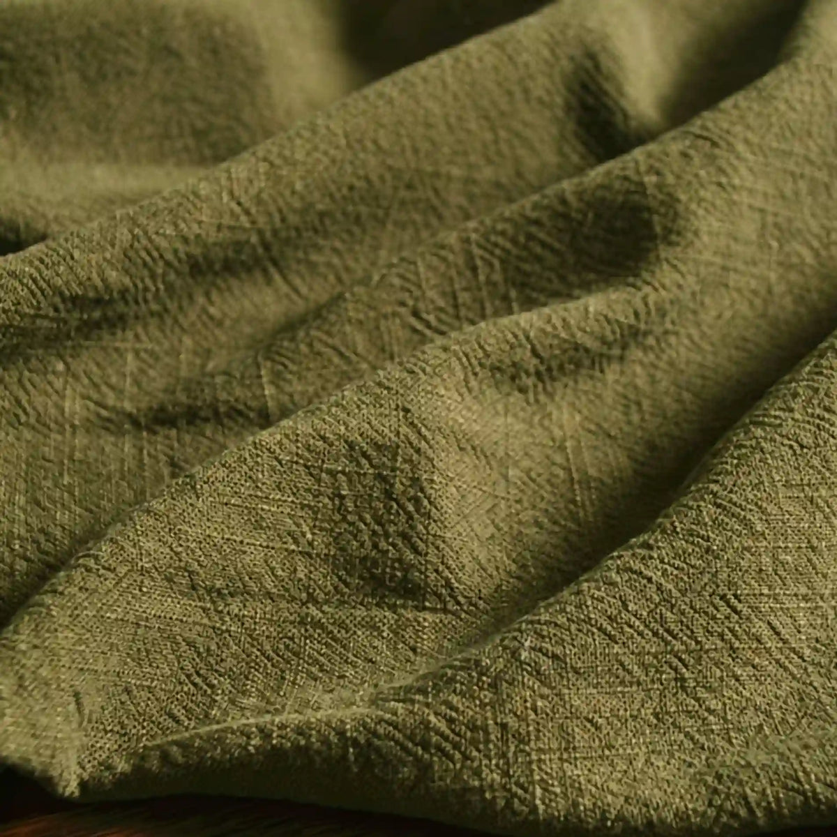 A close-up of Longan Craft's Solid Color Rayon Linen Fabric By The Yard shows soft folds and shadows across its olive green, thick washed slub viscose material, featuring a textured, crinkled surface with visible creases.