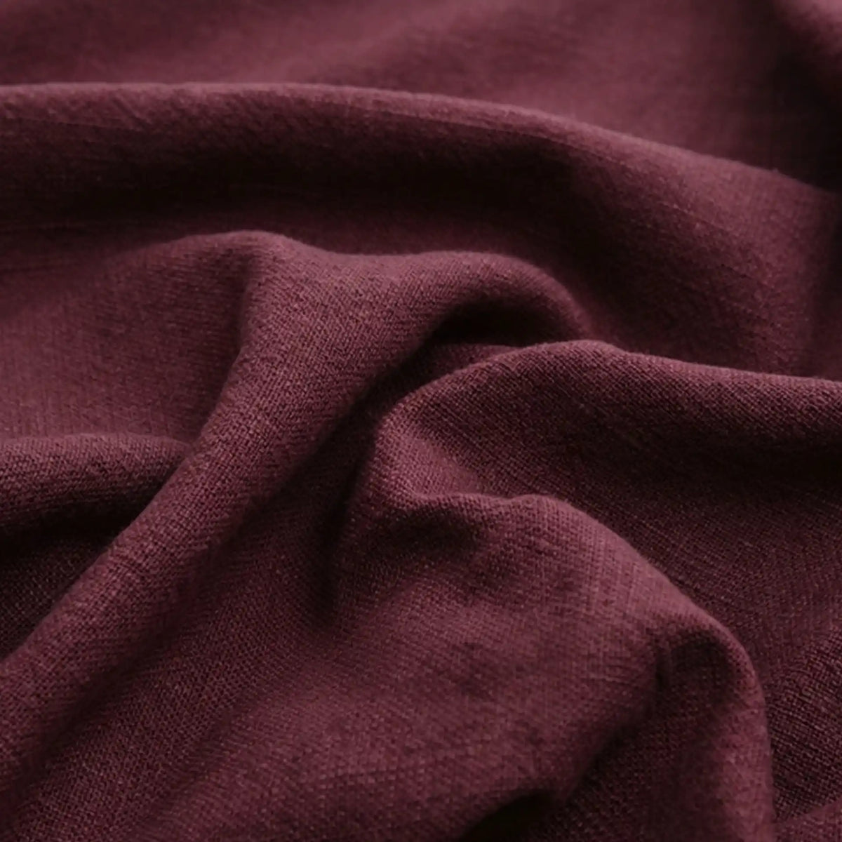 Close-up of Longan Craft's Solid Color Rayon Linen Fabric by the Yard, a thick, washed slub viscose with a soft, textured feel in rich maroon, featuring gentle folds and creases for added depth—perfect for dresses and apparel.