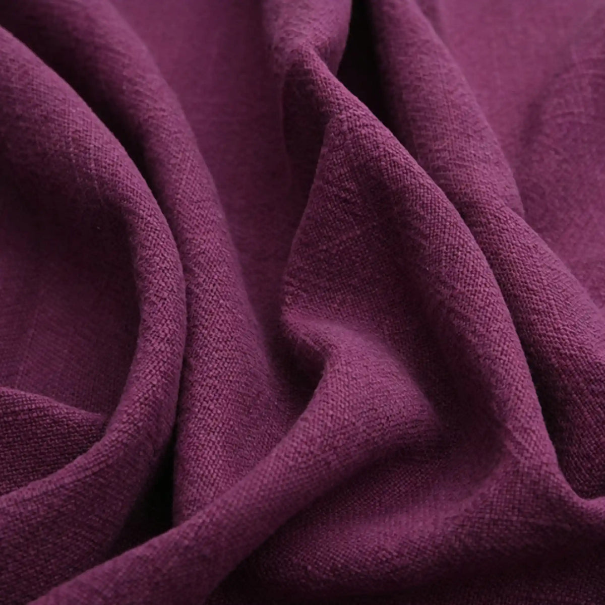 Close-up of Longan Craft's Solid Color Rayon Linen Fabric By The Yard, a thick washed slub viscose material with a soft, textured weave in deep purple and natural folds, perfect for dresses and clothing projects.
