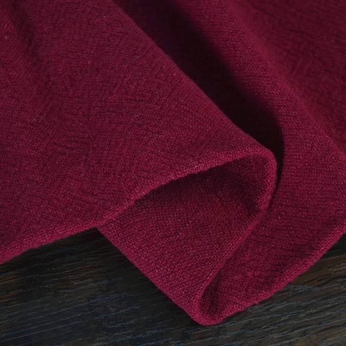 A close-up of Longan Craft's Solid Color Rayon Linen Fabric by the Yard shows the thick, washed slub viscose material in deep red, folded and resting on a dark wooden surface. Perfect for textured, soft dresses and other clothing projects.