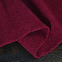 A close-up of Longan Craft's Solid Color Rayon Linen Fabric by the Yard shows the thick, washed slub viscose material in deep red, folded and resting on a dark wooden surface. Perfect for textured, soft dresses and other clothing projects.