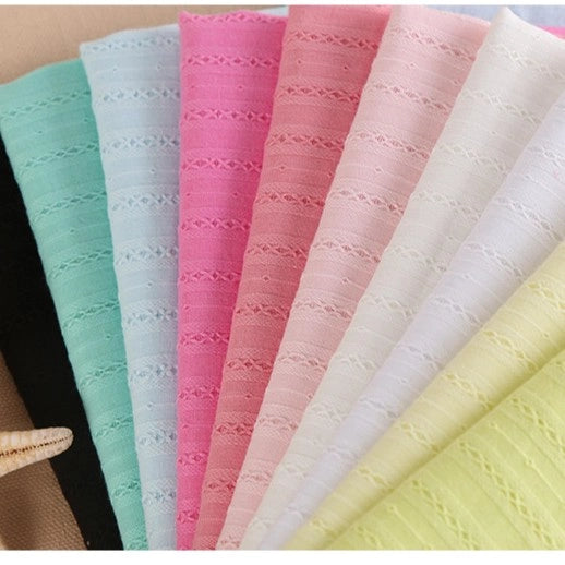 A fan of pastel Solid Color Striped Dobby Cotton Fabric swatches by Longan Craft in black, mint, blue, pink, peach, white, ivory, yellow & light green is arranged on a beige surface—perfect breathable fabric for dressmaking.