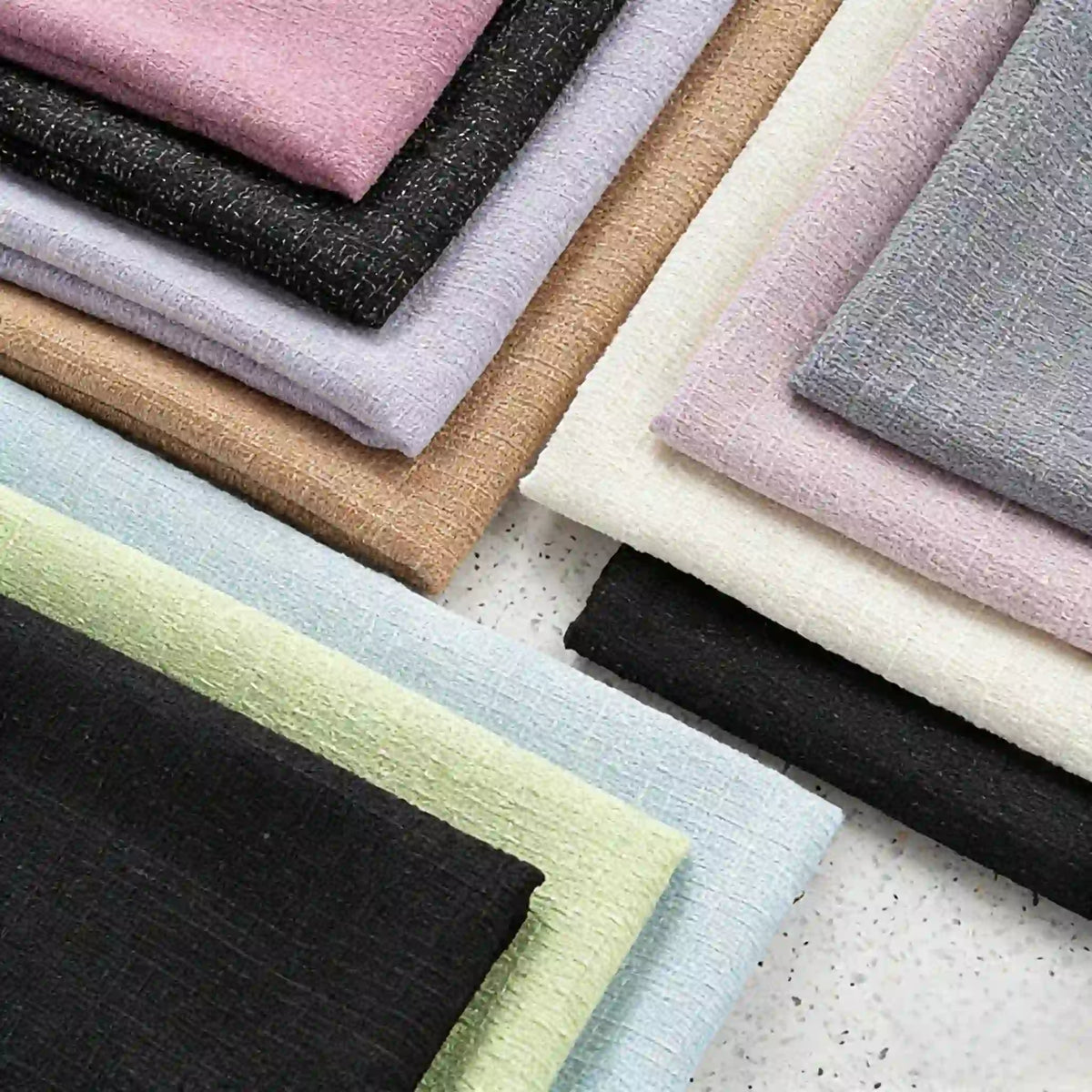 Neatly folded stacks of Longan Craft Solid Color Tweed Fabric By The Yard in black, green, beige, and more, displayed on a white speckled surface—a chic woven polyester tweed textile ideal for suits.