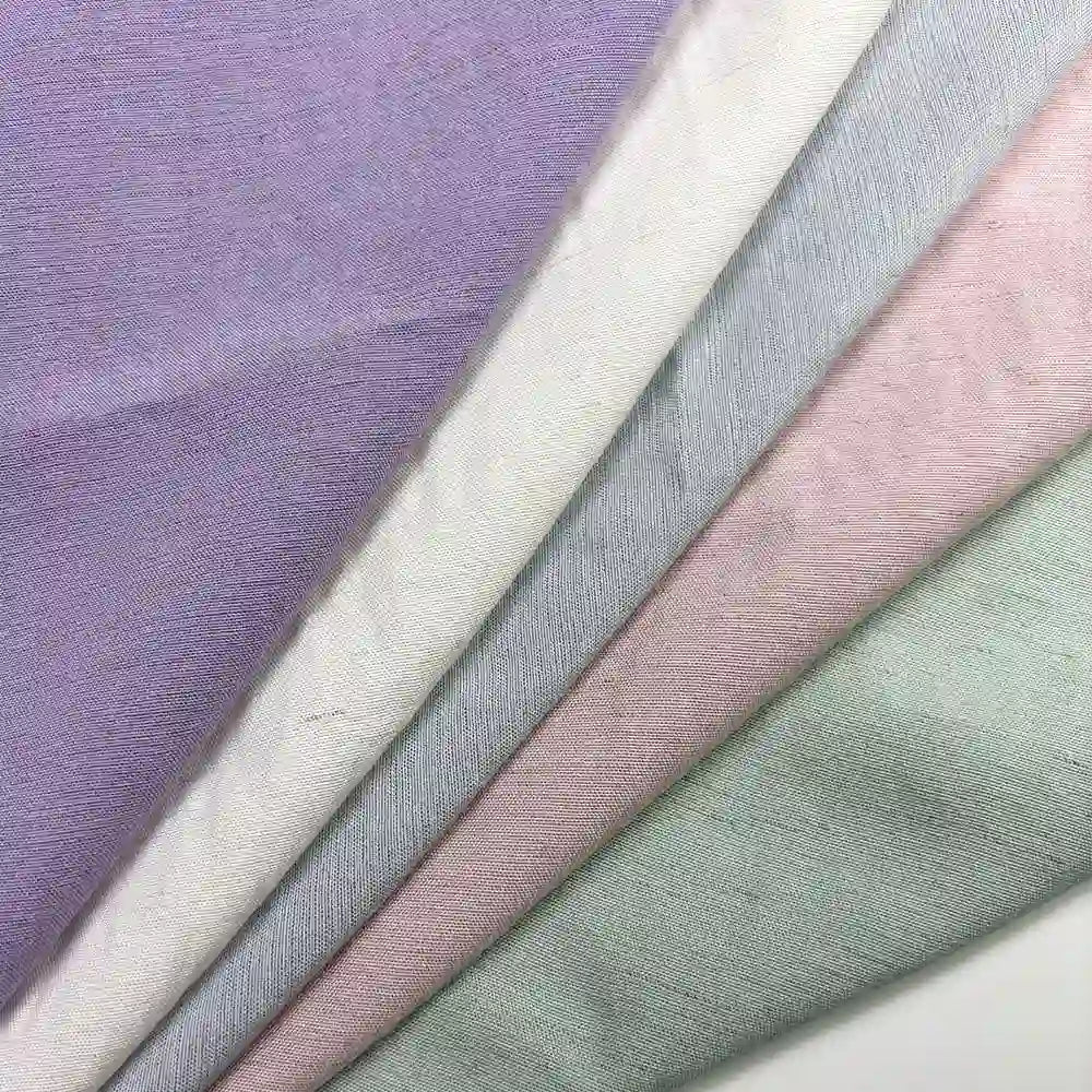 Four pieces of Longan Craft's Solid Color Viscose Lyocell Fabric—pastel lavender, off-white, blush pink, and mint green—are diagonally layered. The eco-friendly rayon-linen blend textile appears smooth, soft, and breathable.