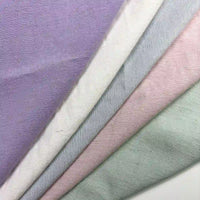 Four pieces of Longan Craft's Solid Color Viscose Lyocell Fabric—pastel lavender, off-white, blush pink, and mint green—are diagonally layered. The eco-friendly rayon-linen blend textile appears smooth, soft, and breathable.