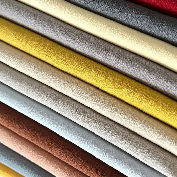A close-up of neatly stacked rolls of Solid Color Washed Crepe Fabric By The Yard from Longan Craft, displayed in various colors such as yellow, gray, brown, cream, and red, highlighting the soft textured 100% cotton crepe material suitable for pants.