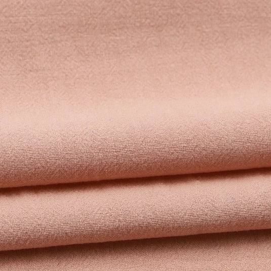 Close-up of Longan Craft’s Solid Color Washed Crepe Fabric By The Yard, a soft, light pink 100% cotton material featuring a slightly textured crepe surface and neatly folded in horizontal layers—ideal for pants and clothing projects.