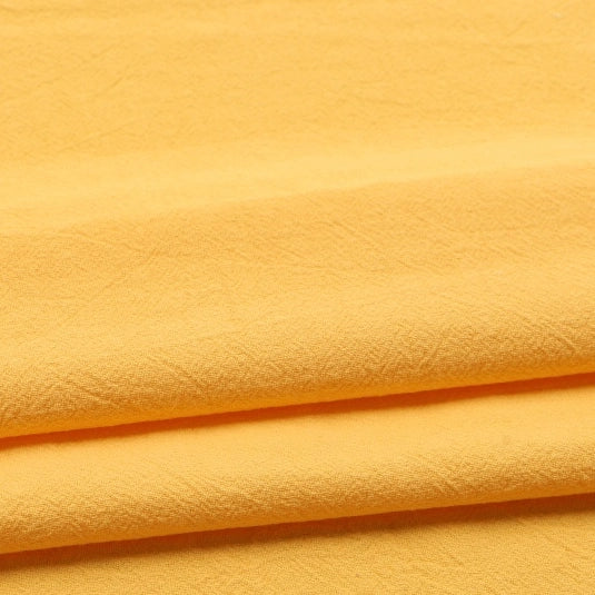 Three layers of the Longan Craft Solid Color Washed Crepe Fabric by the Yard, made from 100% cotton, are neatly folded. This pale yellow fabric features a soft, textured crepe surface with gentle creases throughout. Under the lighting, its smooth and slightly matte finish is accentuated.