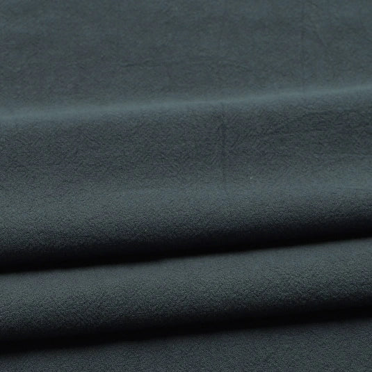 Close-up of folded Solid Color Washed Crepe Fabric by the yard from Longan Craft, made from 100% cotton with a soft, slightly textured crepe surface in dark gray, displaying subtle creases—ideal for pants and other clothing projects.