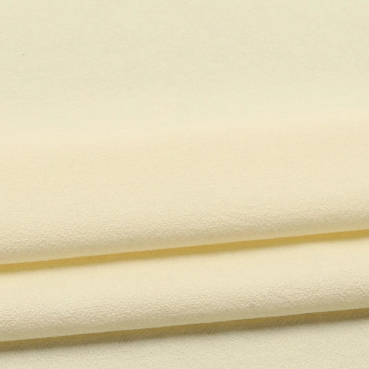 Close-up of neatly folded Longan Craft Solid Color Washed Crepe Fabric by the yard in pale yellow, made from 100% cotton with a soft textured surface, displaying gentle shadows and subtle creases along the edges.