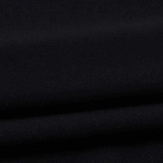 A close-up of Longan Craft’s Solid Color Washed Crepe Fabric By The Yard, crafted from 100% cotton crepe for clothing, showcases its smooth, matte black surface with gentle folds and a soft, textured finish that creates delicate shadows and highlights.
