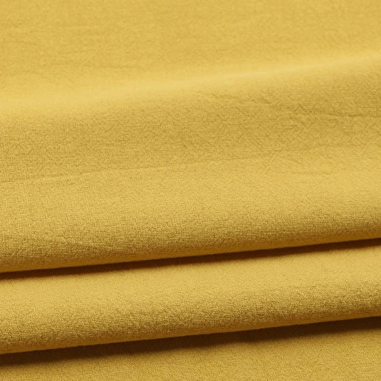 Close-up of folded Solid Color Washed Crepe Fabric By The Yard from Longan Craft in a mustard yellow hue, crafted from 100% cotton. The soft, lightly textured surface of this crepe clothing material creates gentle shadows as it folds, highlighting its smooth and lightweight quality—ideal for sewing pants and garments.