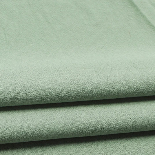 Close-up of three neatly folded layers of Longan Craft Solid Color Washed Crepe Fabric By The Yard, made from 100% cotton. This light green fabric features a soft, slightly textured surface and appears smooth and lightweight—ideal for pants, clothing, or home textiles.