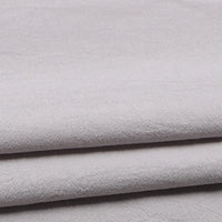 Close-up of folded Longan Craft Solid Color Washed Crepe Fabric by the Yard, made from 100% cotton. The light gray material features a soft, gently textured surface and a subtle crepe weave pattern, appearing smooth and neatly stacked—ideal for clothing or pants.