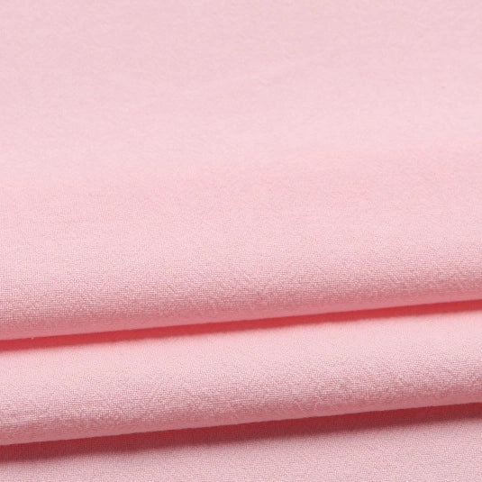 A close-up of folded Longan Craft Solid Color Washed Crepe Fabric by the yard, made from 100% cotton crepe in light pink, highlighting its soft and textured finish—ideal for pants and clothing material.