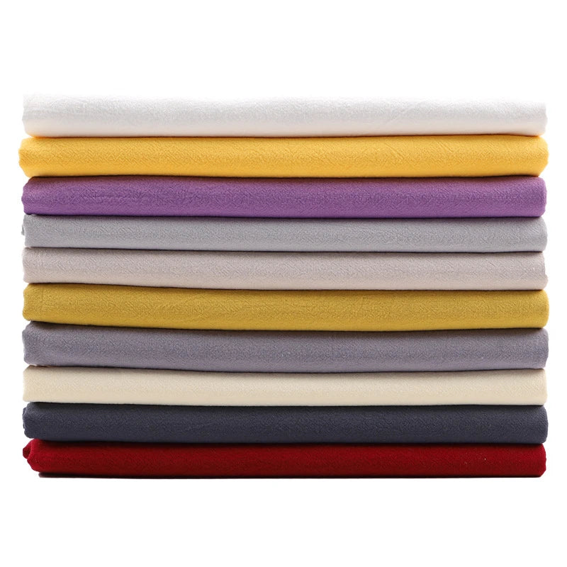 A neat horizontal stack of Longan Craft Solid Color Washed Crepe Fabric by the yard, made from 100% cotton, is displayed in an array of colors—white, yellow, purple, gray, beige, black, and red—against a white background. The soft textured crepe fabric is ideal for making pants and other clothing projects.