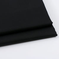 A close-up of Solid Color Wool Gabardine Fabric by Longan Craft, a black rayon polyester blended twill ideal for casual wear, shown folded on a white surface.