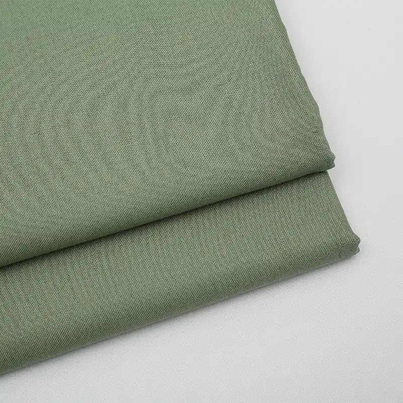 Two pieces of Longan Craft Solid Color Wool Gabardine Fabric by the yard in light olive green are neatly folded on a white surface. This rayon polyester blended twill is smooth, subtly textured, and ideal for casual wear.