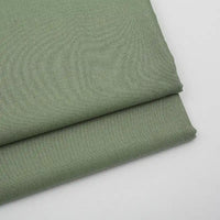 Two pieces of Longan Craft Solid Color Wool Gabardine Fabric by the yard in light olive green are neatly folded on a white surface. This rayon polyester blended twill is smooth, subtly textured, and ideal for casual wear.