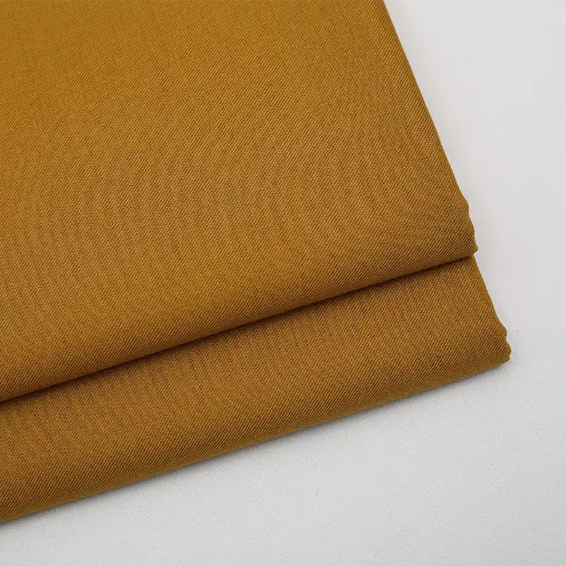 Two neatly folded pieces of Longan Craft’s Solid Color Wool Gabardine Fabric By The Yard, a rayon polyester blended twill ideal for casual wear, in mustard yellow are placed on a white surface.