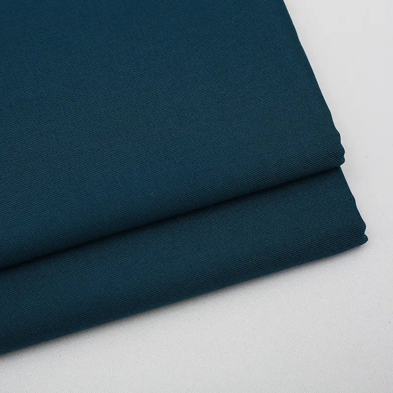 Two neatly folded pieces of Longan Craft Solid Color Wool Gabardine Fabric rest on a light surface, showcasing the smooth, slightly textured rayon-polyester blended twill—ideal for casual wear.