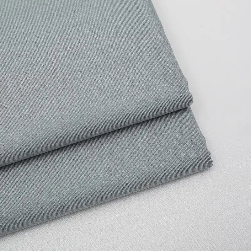 Two pieces of Longan Craft Solid Color Wool Gabardine Fabric are neatly folded on a white surface, displaying a smooth, soft texture. This rayon polyester blended twill is ideal for casual wear and sold by the yard.