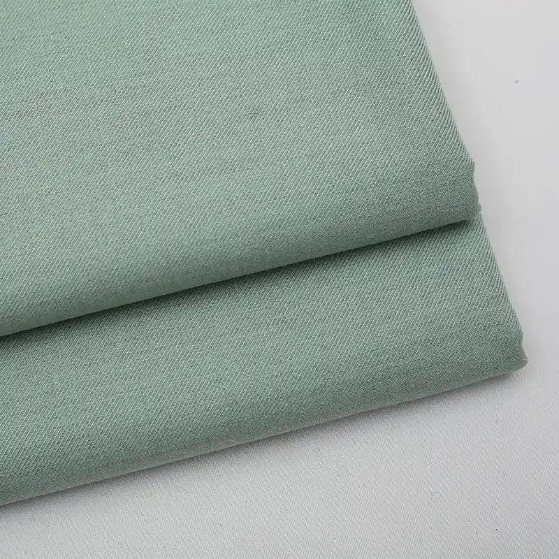 A close-up of two neatly folded pieces of Longan Craft’s Solid Color Wool Gabardine Fabric By The Yard, a rayon polyester blended twill gabardine textile with a fine, slightly textured weave, displayed on a white surface.