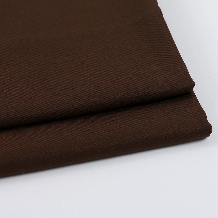 A close-up of two folded pieces of Longan Craft's Solid Color Wool Gabardine Fabric by the yard, a smooth and tightly woven rayon polyester blend twill, stacked on a white surface—ideal for casual wear.