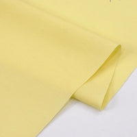 A neatly folded sheet of Longan Craft Solid Cotton Lawn Fabric By The Yard sits on a white surface, highlighting its smooth texture and soft light yellow hue—perfect for cozy lawn dress creations.