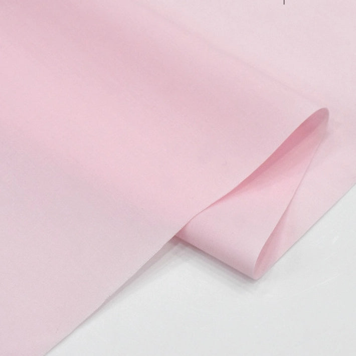 A close-up of Longan Craft's Solid Cotton Lawn Fabric by the yard, a light pink polyester lawn cloth material for cozy dressmaking, neatly folded and displayed on a white surface.