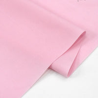 A close-up of Longan Craft’s Solid Cotton Lawn Fabric By The Yard shows the smooth, soft polyester lawn cloth material in light pink, neatly folded with a matte finish—ideal for cozy lawn dress fabric.