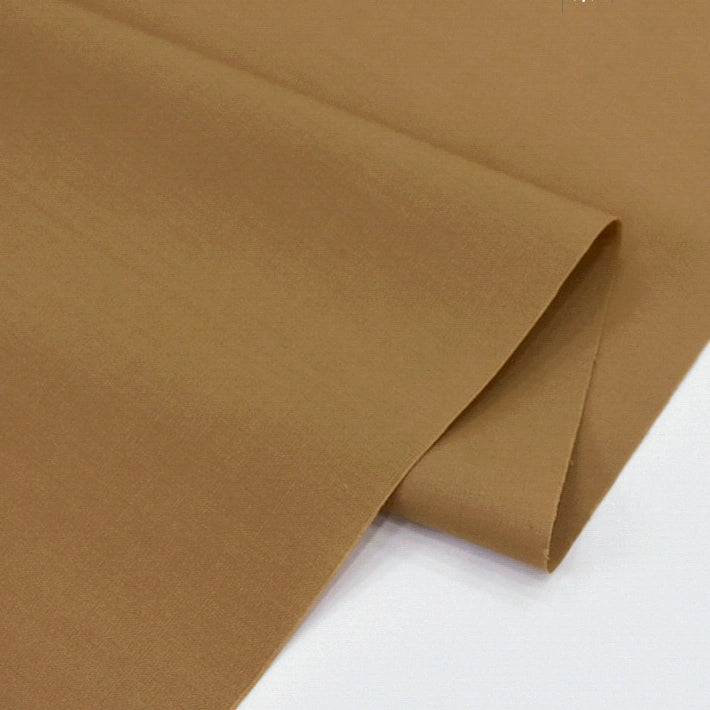 Longan Craft's Solid Cotton Lawn Fabric by the yard, a light brown polyester lawn cloth, is shown laid flat with a folded corner to highlight its smooth, cozy texture—ideal for comfortable dressmaking and versatile sewing projects.