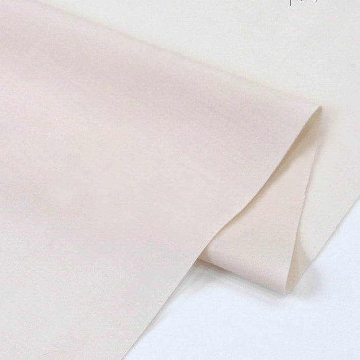 A close-up of Longan Craft's Solid Cotton Lawn Fabric by the Yard, a light beige blended cotton-polyester lawn cloth partially folded on a white surface, revealing its smooth and soft texture—ideal for cozy dresses.