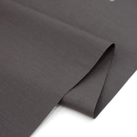 A close-up of Longan Craft's Solid Cotton Lawn Fabric By The Yard shows its smooth, dark gray polyester-cotton material, partially folded on a white surface—ideal cozy lawn dress fabric.