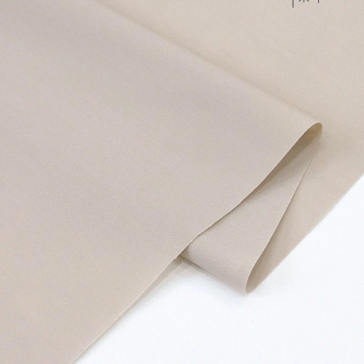 A close-up of two overlapping pieces of Longan Craft Solid Cotton Lawn Fabric by the yard, a smooth, light beige polyester-cotton lawn cloth material, neatly folded on a flat surface.