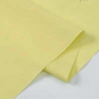 A close-up of Longan Craft's Solid Cotton Lawn Fabric By The Yard, a smooth light yellow polyester-cotton lawn cloth material, neatly folded with soft shadows accentuating its cozy texture.