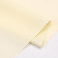 A close-up of Solid Cotton Lawn Fabric by the yard from Longan Craft, a cozy cream-colored blended cotton polyester lawn cloth, partially folded on a plain white surface.