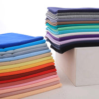 Neatly folded stacks of Longan Craft's Spandex Jersey Fabric By The Yard—solid color cotton jersey with a soft, stretchy feel—are arranged on a white surface in various vibrant shades.