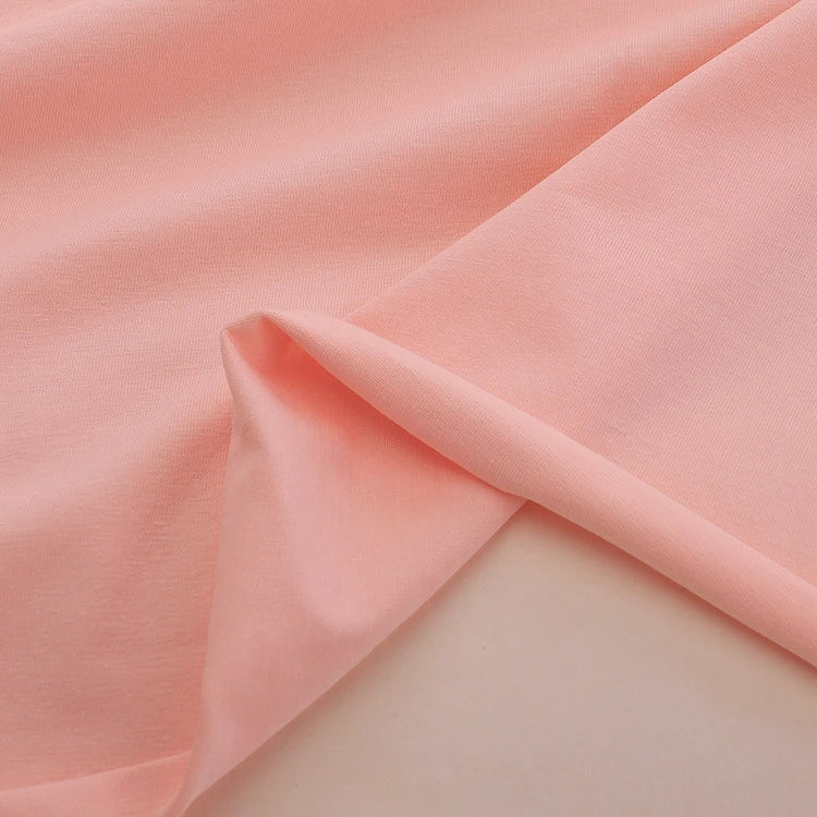 A close-up of Longan Craft's Spandex Jersey Fabric By The Yard highlights its soft, light pink cotton jersey, smooth texture, gentle drape, and impressive four-way stretch—ideal for dresses and more.