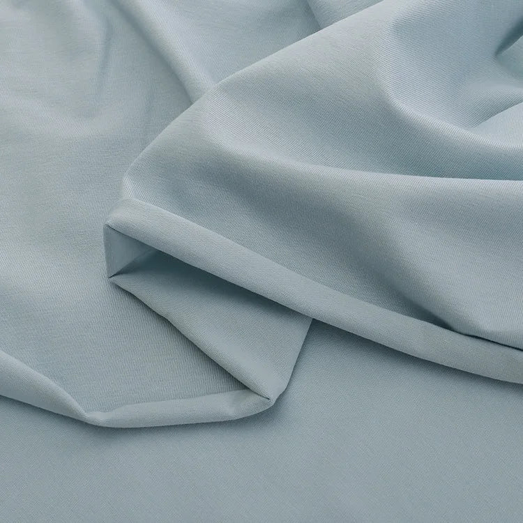 A close-up of Longan Craft’s Spandex Jersey Fabric By The Yard in light blue, featuring soft folds, smooth texture, and four-way stretch that creates gentle shadows and highlights. Perfect solid color cotton jersey fabric for dresses.