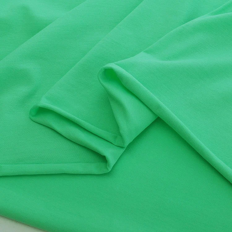 Longan Craft’s Elastane Jersey Fabric By The Yard in bright green features a smooth, stretchy texture and is shown neatly folded with soft creases and overlapping layers on a matching background.