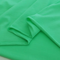 Longan Craft’s Elastane Jersey Fabric By The Yard in bright green features a smooth, stretchy texture and is shown neatly folded with soft creases and overlapping layers on a matching background.