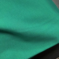 A close-up of Longan Craft's Spandex Jersey Fabric By The Yard in bright green, featuring subtle wrinkles, a soft texture, and four-way stretch as it rests on a dark surface.