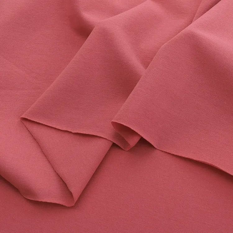 A close-up of Longan Craft’s Spandex Jersey Fabric By The Yard in soft coral pink, highlighting its smooth texture, comfortable four-way stretch, and gentle drape—ideal for dresses and apparel.