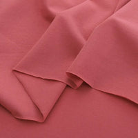 A close-up of Longan Craft’s Spandex Jersey Fabric By The Yard in soft coral pink, highlighting its smooth texture, comfortable four-way stretch, and gentle drape—ideal for dresses and apparel.