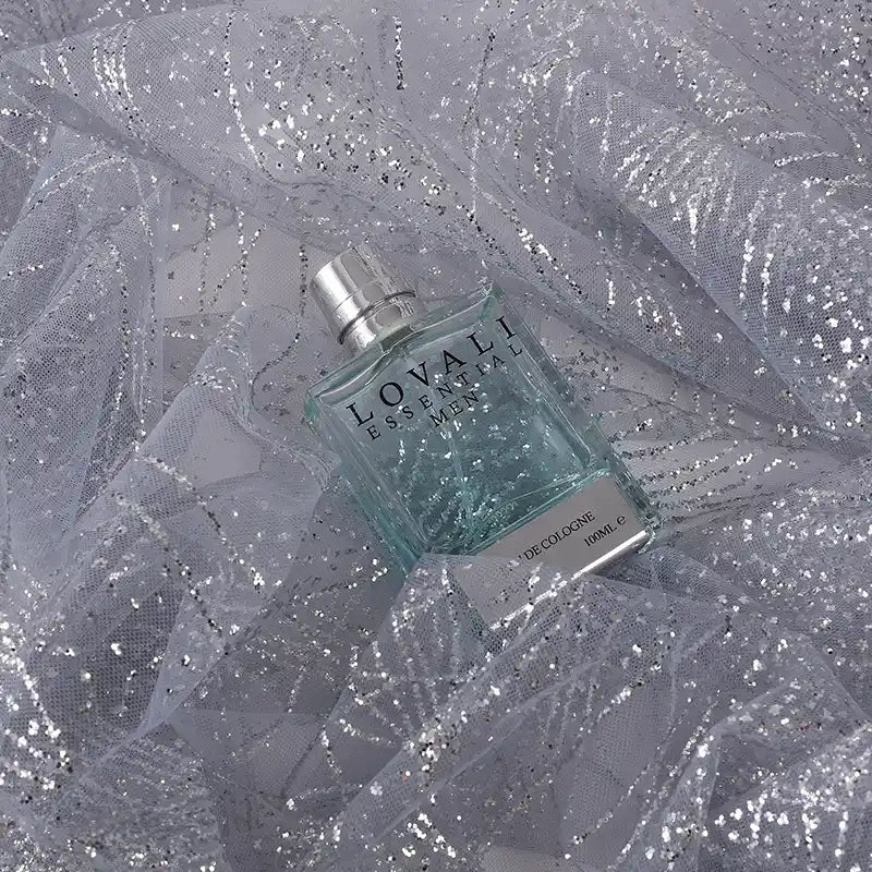 A bottle of LOVALI essential eau de cologne rests on Longan Craft’s Sparkle Glitter Tulle Fabric By The Yard—multicolor, shiny, and delicate tulle ideal for evening gowns—creating a shimmering, elegant backdrop.